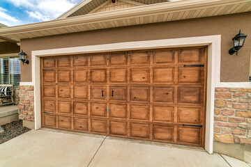 Wide brown wooden panelled garage door of an attached garage with wall lamps