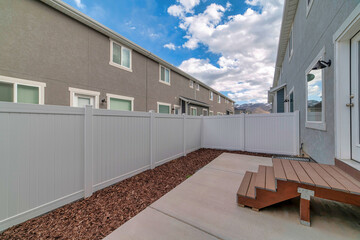 Fully fenced backyard of two storey home with wooden steps leading to glass door