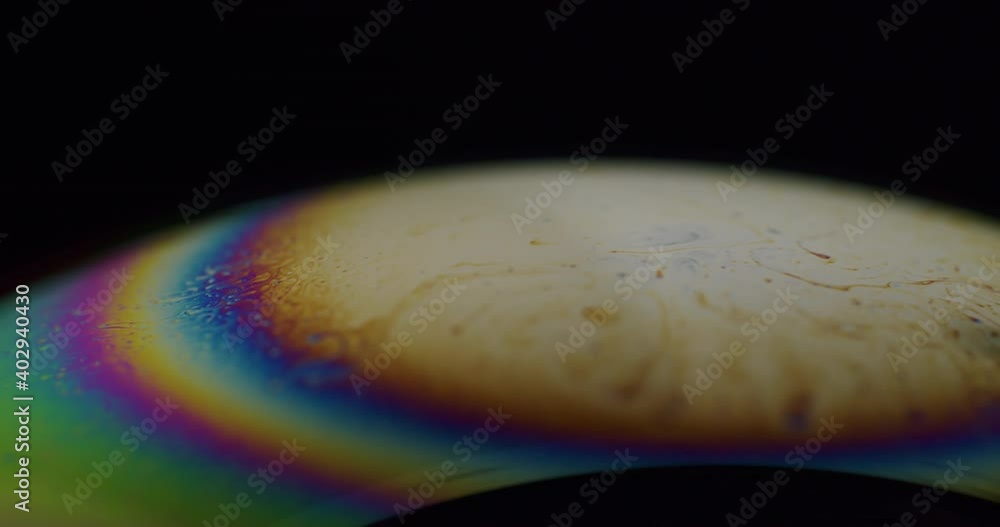 Poster macro shot of a soap bubble with rainbow colored strips on the edge of the pole. sphere moving slowl
