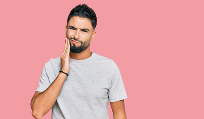 Young man with beard wearing casual grey tshirt touching mouth with hand with painful expression because of toothache or dental illness on teeth. dentist