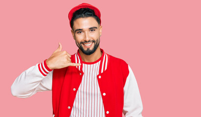 Young man with beard wearing baseball uniform smiling doing phone gesture with hand and fingers like talking on the telephone. communicating concepts.