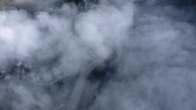 Aerial: top down view over cloudy karst mountains, remote Chinese town