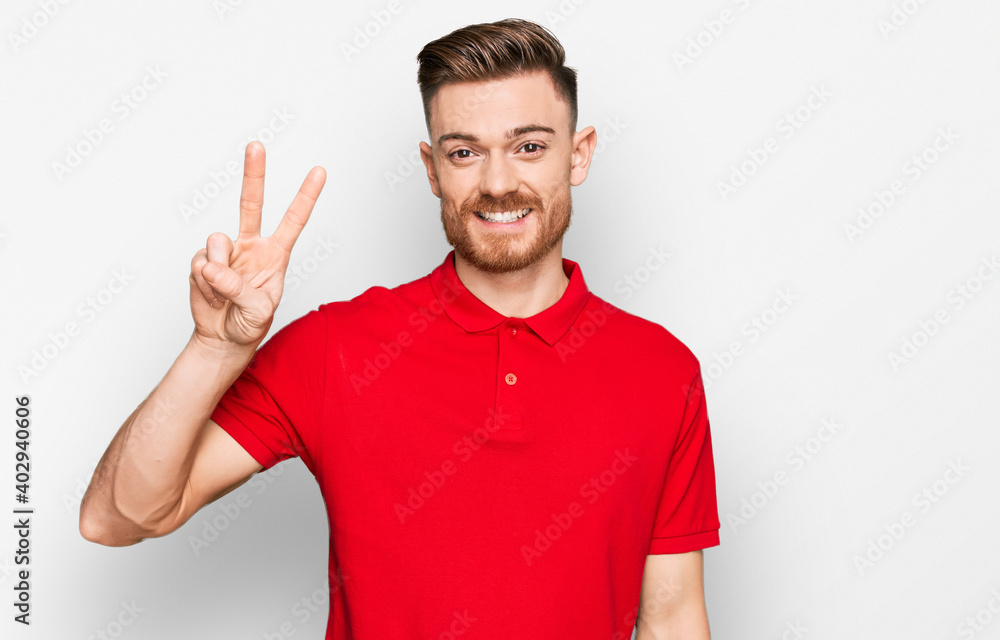 Wall mural young redhead man wearing casual clothes showing and pointing up with fingers number two while smili