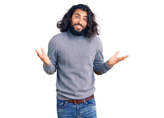 Young arab man wearing casual clothes clueless and confused expression with arms and hands raised....