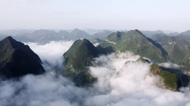 Asian karst mountains rising above misty clouds in remote China, aerial view