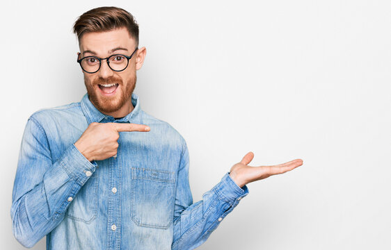 Young redhead man wearing casual denim shirt amazed and smiling to the camera while presenting with hand and pointing with finger.