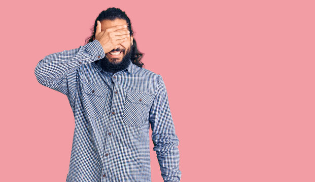 Young arab man wearing casual clothes smiling and laughing with hand on face covering eyes for surprise. blind concept.