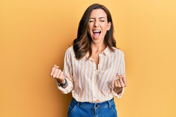 Young brunette woman wearing casual clothes over yellow background celebrating surprised and amazed for success with arms raised and eyes closed