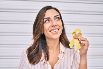 Young hispanic woman smiling happy holding awareness yellow ribon standing at the city.