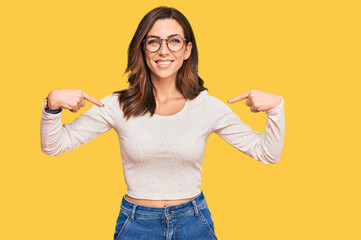 Young brunette woman wearing casual clothes and glasses looking confident with smile on face,...