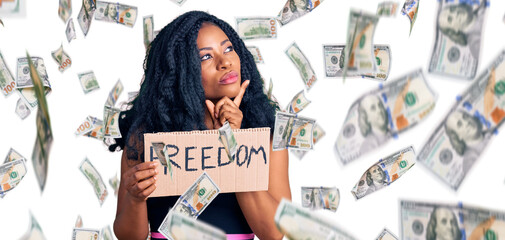 Beautiful african american woman holding freedom banner serious face thinking about question with hand on chin, thoughtful about confusing idea