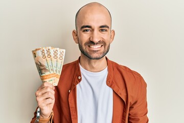 Young hispanic man holding 500 norwegian krone banknotes looking positive and happy standing and...