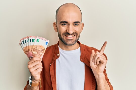Young hispanic man holding bunch of 10 euro banknotes smiling happy pointing with hand and finger to the side