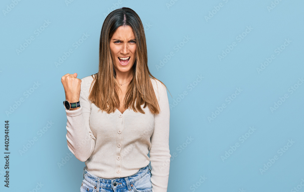 Wall mural Young woman wearing casual clothes angry and mad raising fist frustrated and furious while shouting with anger. rage and aggressive concept.