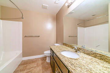 Built in bathtub in front of toilet and sink with marble countertop and cabinets