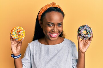 Young african woman holding tasty colorful doughnuts winking looking at the camera with sexy...