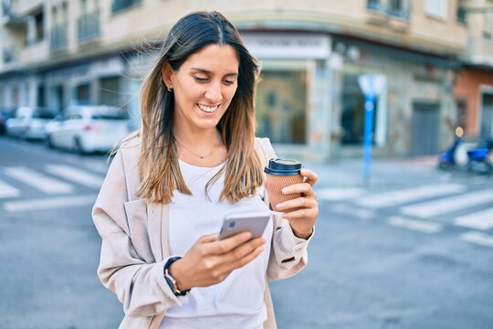 Young caucasian woman smiling happy using smartphone and drinking take away coffee at the city.