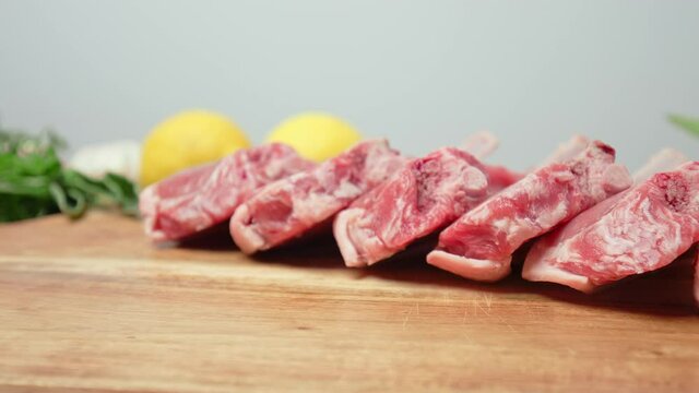 Close-up raw chopped lamb ribs on cutting board with decorative vegetables in 4K. Concept of fresh redraw lamb cutlets sliced from a rack with bones nicely arranged on the table in slow-motion.