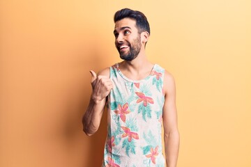 Young handsome man with beard wearing summer sleeveless t-shirt pointing thumb up to the side...