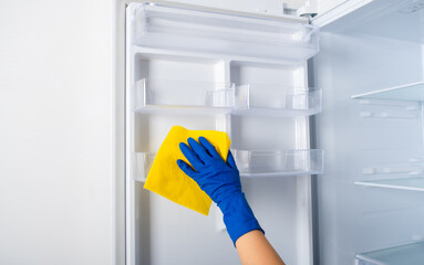 A woman's hand in a blue rubber protective glove and a yellow rag washes and cleans the...