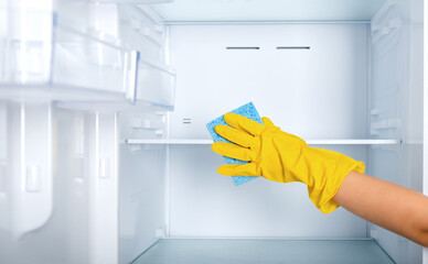 A woman's hand in a yellow rubber protective glove and a blue sponge washes and cleans the...