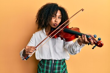 Beautiful african american woman with afro hair playing classical violin looking at the camera...