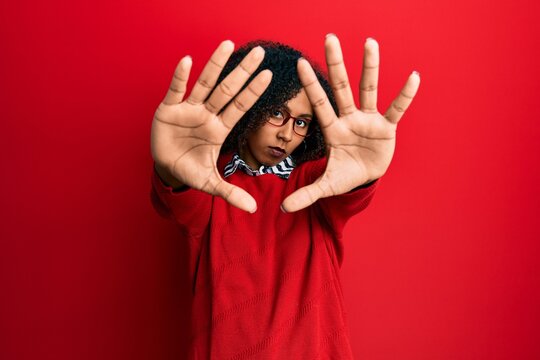 Beautiful african american woman with afro hair wearing sweater and glasses doing frame using hands palms and fingers, camera perspective