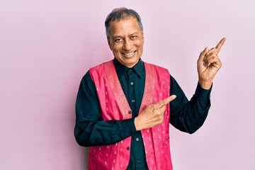 Middle age indian man wearing traditional indian clothes smiling and looking at the camera pointing...