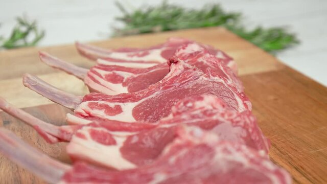 Close-up raw chopped lamb ribs on cutting board with decorative vegetables in 4K. Concept of fresh redraw lamb cutlets sliced from a rack with bones nicely arranged on the table in slow-motion.