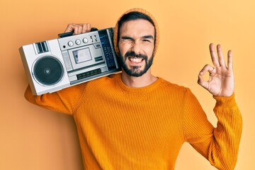 Young hispanic man holding boombox, listening to music doing ok sign with fingers, smiling friendly gesturing excellent symbol