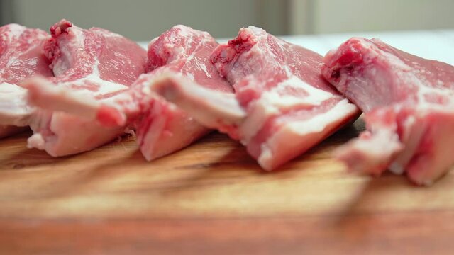 Close-up raw chopped lamb ribs on cutting board with decorative vegetables in 4K. Concept of fresh redraw lamb cutlets sliced from a rack with bones nicely arranged on the table in slow-motion.