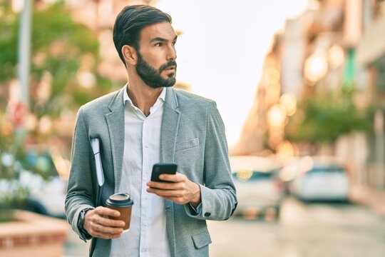 Young hispanic businessman with serious expression using smartphone and drinking coffee at the city.