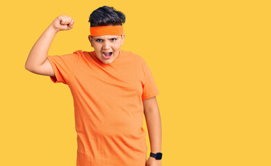 Little boy kid wearing sportswear angry and mad raising fist frustrated and furious while shouting with anger. rage and aggressive concept.