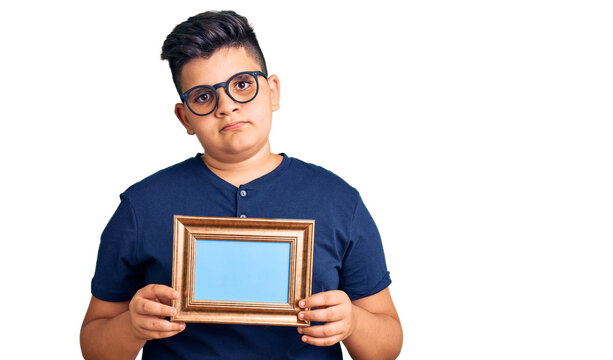 Little boy kid holding empty frame thinking attitude and sober expression looking self confident