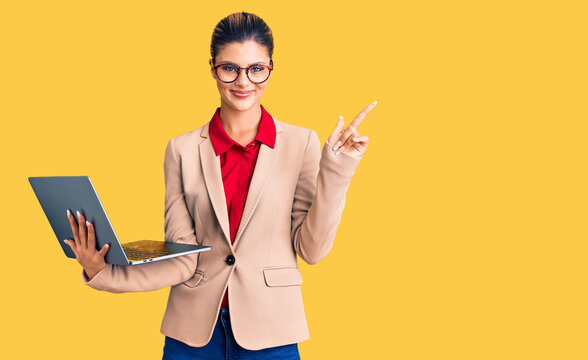 Young beautiful woman holding laptop smiling happy pointing with hand and finger to the side