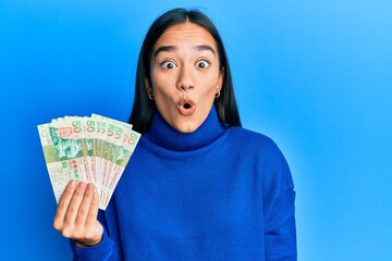Young asian woman holding 50 hong kong dollars banknotes scared and amazed with open mouth for...