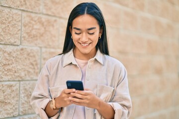 Young latin girl smiling happy using smartphone at the city.
