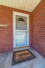 Gray front door and glass storm door at the entrance of home with red brick wall