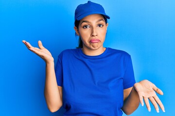 Beautiful brunette woman wearing delivery uniform clueless and confused expression with arms and hands raised. doubt concept.