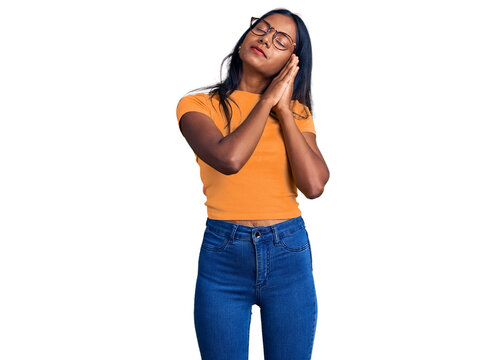 Young indian girl wearing casual clothes and glasses sleeping tired dreaming and posing with hands together while smiling with closed eyes.
