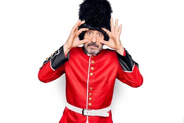 Middle age handsome wales guard man wearing traditional uniform over white background Trying to open eyes with fingers, sleepy and tired for morning fatigue