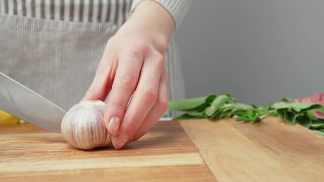 Chef peeling garlic close-up and taking off the skin then slicing in half in 4K. Concept of a woman chef peeling a bunch of garlic and cutting apart.