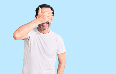 Fototapeta premium Middle age handsome man wearing casual t-shirt smiling and laughing with hand on face covering eyes for surprise. blind concept.