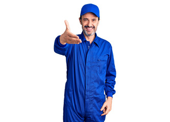 Middle age handsome man wearing mechanic uniform smiling friendly offering handshake as greeting and welcoming. successful business.