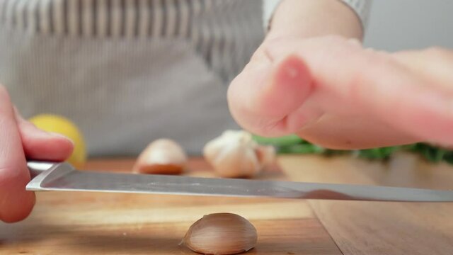 Chef crushing garlic close-up and squeeze with a side knife in 4K. Concept of a woman chef squeezing a bunch of garlic with hand on a cutting board in slow-motion.