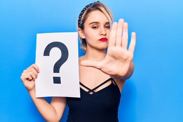 Young beautiful blonde woman holding question mark with open hand doing stop sign with serious and confident expression, defense gesture
