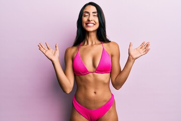 Beautiful hispanic woman wearing bikini celebrating mad and crazy for success with arms raised and...