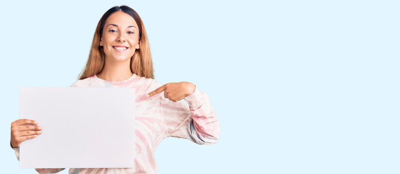 Beautiful young woman holding blank empty banner pointing finger to one self smiling happy and proud