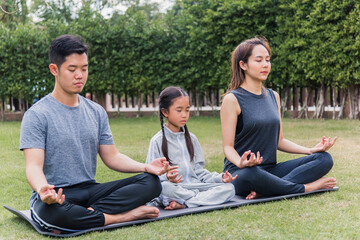 Asian young mother, father practicing doing yoga exercises with child daughter outdoors in meditate pose together in nature a field garden park, family kid sport and exercises for healthy lifestyle