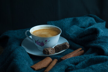 Coffee in a white cup decorated with cinnamon and 2 chocolates and a sweater as the base